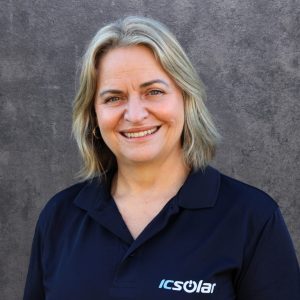 Portrait of a smiling woman in a navy ICSolar polo against a gray textured backdrop.