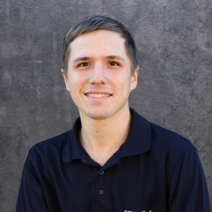 Smiling man with short light brown hair in a navy polo against a gray textured wall.